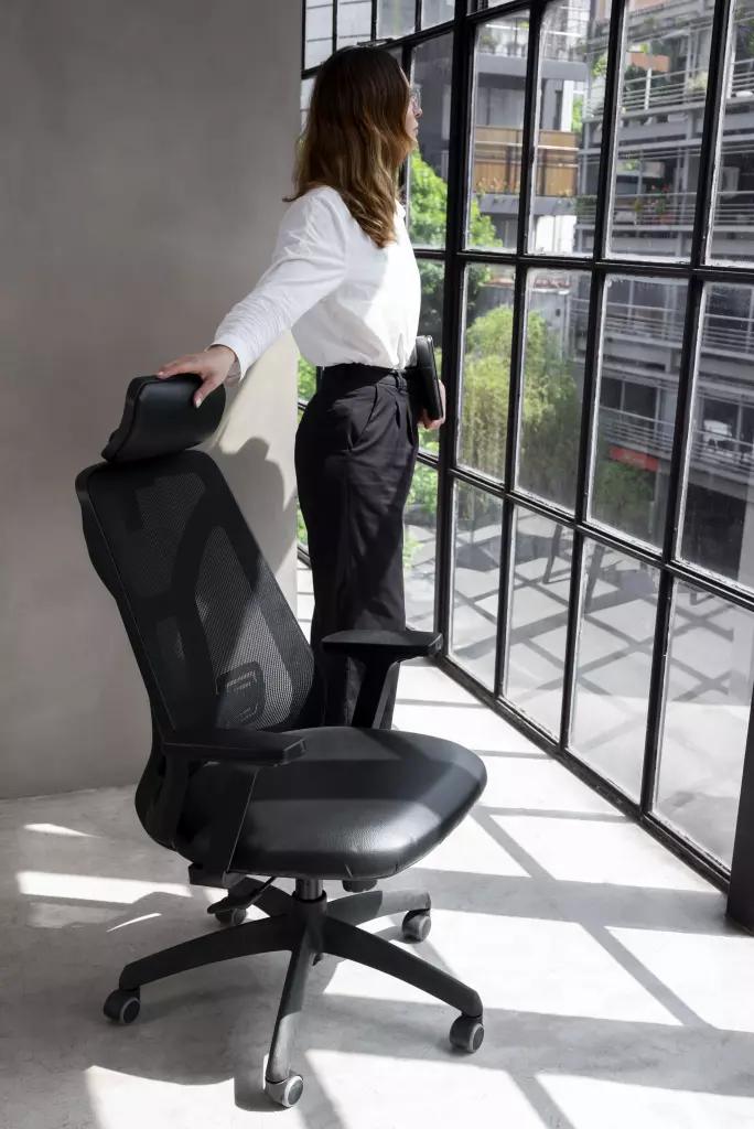 A woman in business attire stands beside a black ergonomic office chair; a must-have office chair.